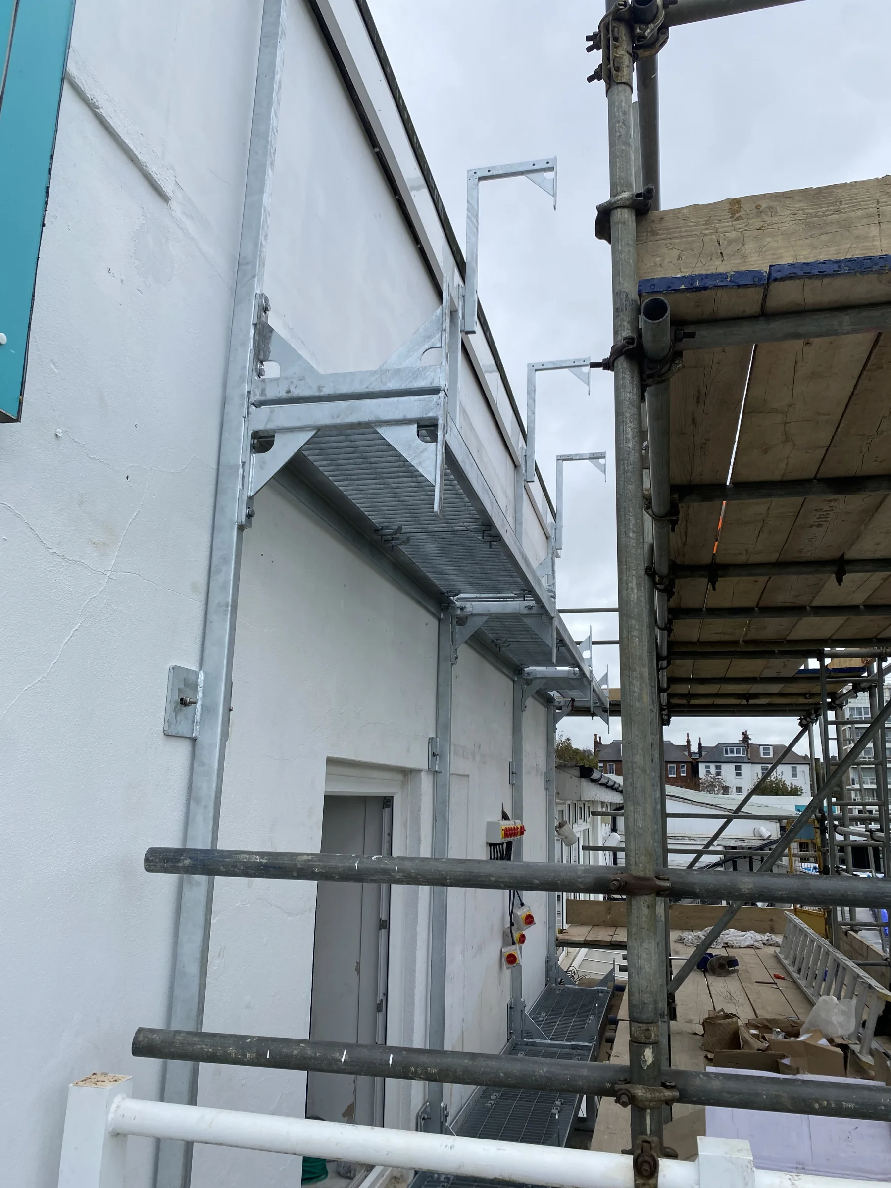 Brighton Cricket — close-up of galvanised cantilever brackets and grating walkway fixed to pavilion wall, supporting future LED scoreboard