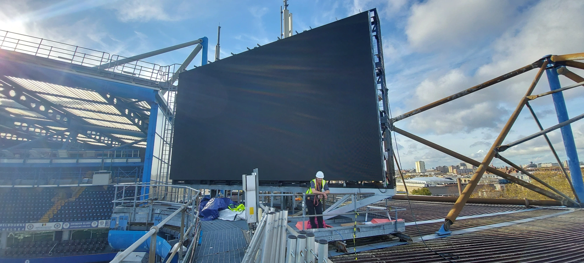 Chelsea FC — large-format LED screen mounted to roofline support frame at Stamford Bridge with engineer commissioning at high level