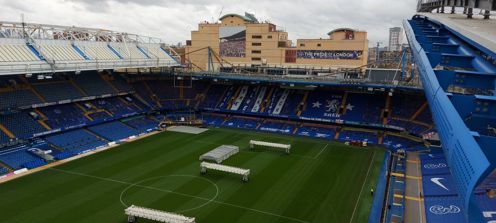 Chelsea FC — wide elevated view across Stamford Bridge stadium bowl with pitchside truss equipment in place ahead of fixture turnaround