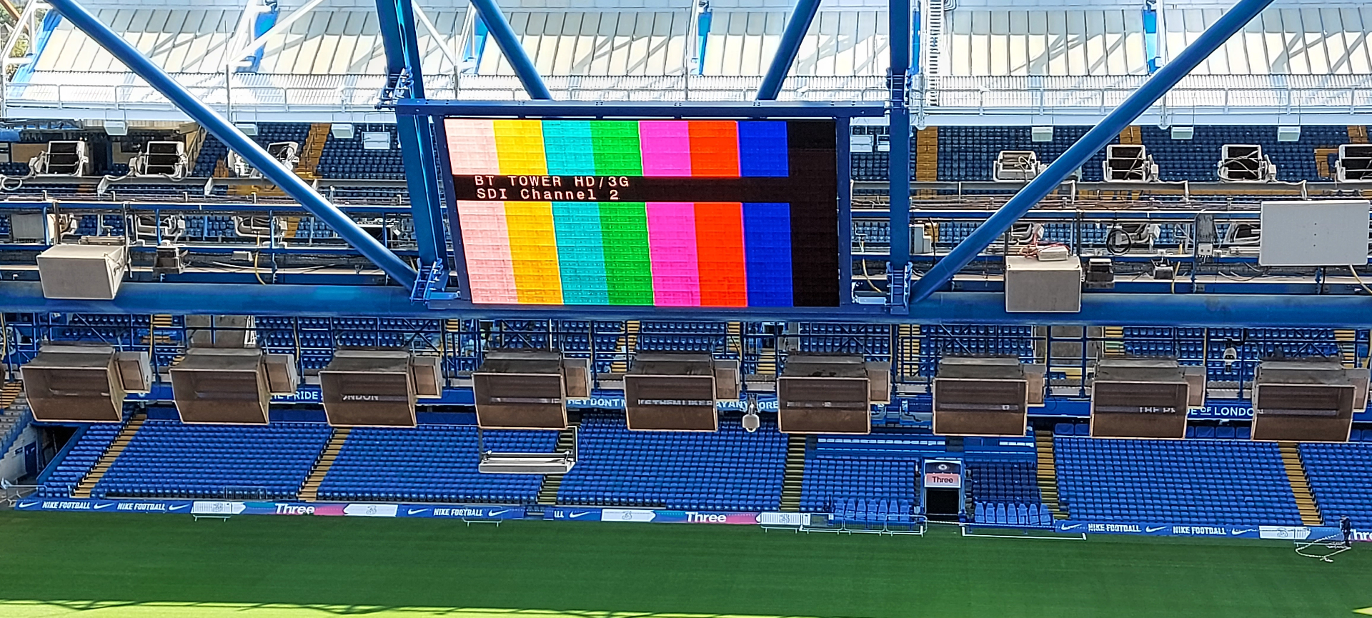 Chelsea FC — close-up of suspended LED scoreboard showing SMPTE colour bars and BT Tower HD/3G SDI Channel 2 feed identifier during signal test