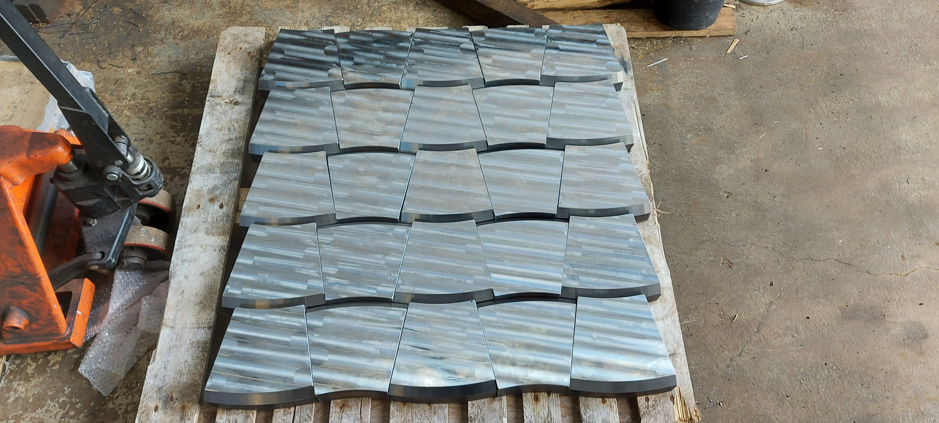 CNC — pallet of machined curved steel tile components arranged in staggered rows, showing parallel toolpath finish across batch